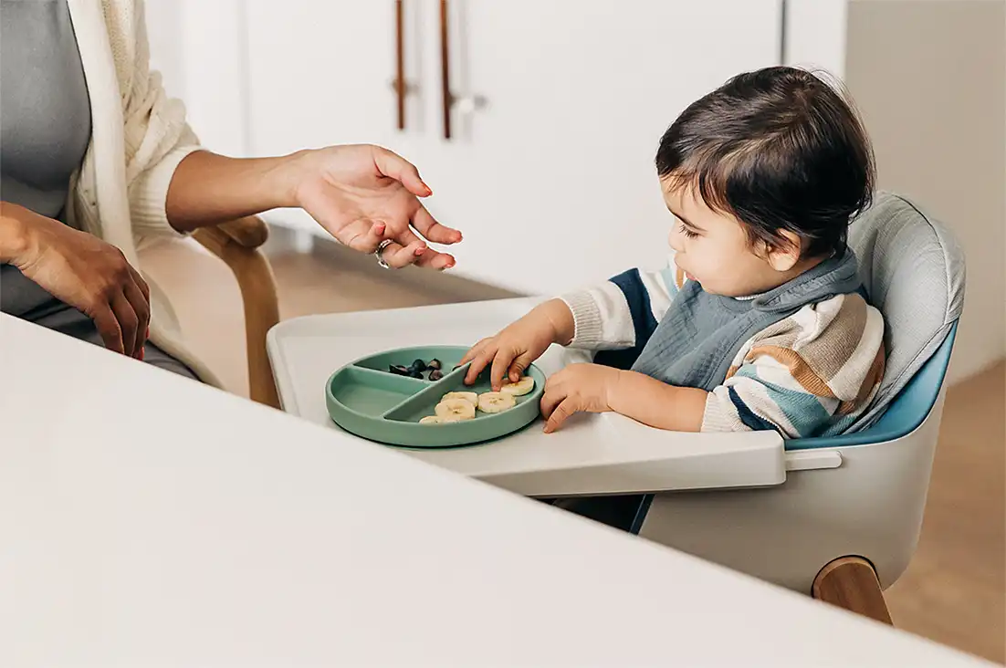 Child touches their food while sitting in the cushion of their high chair