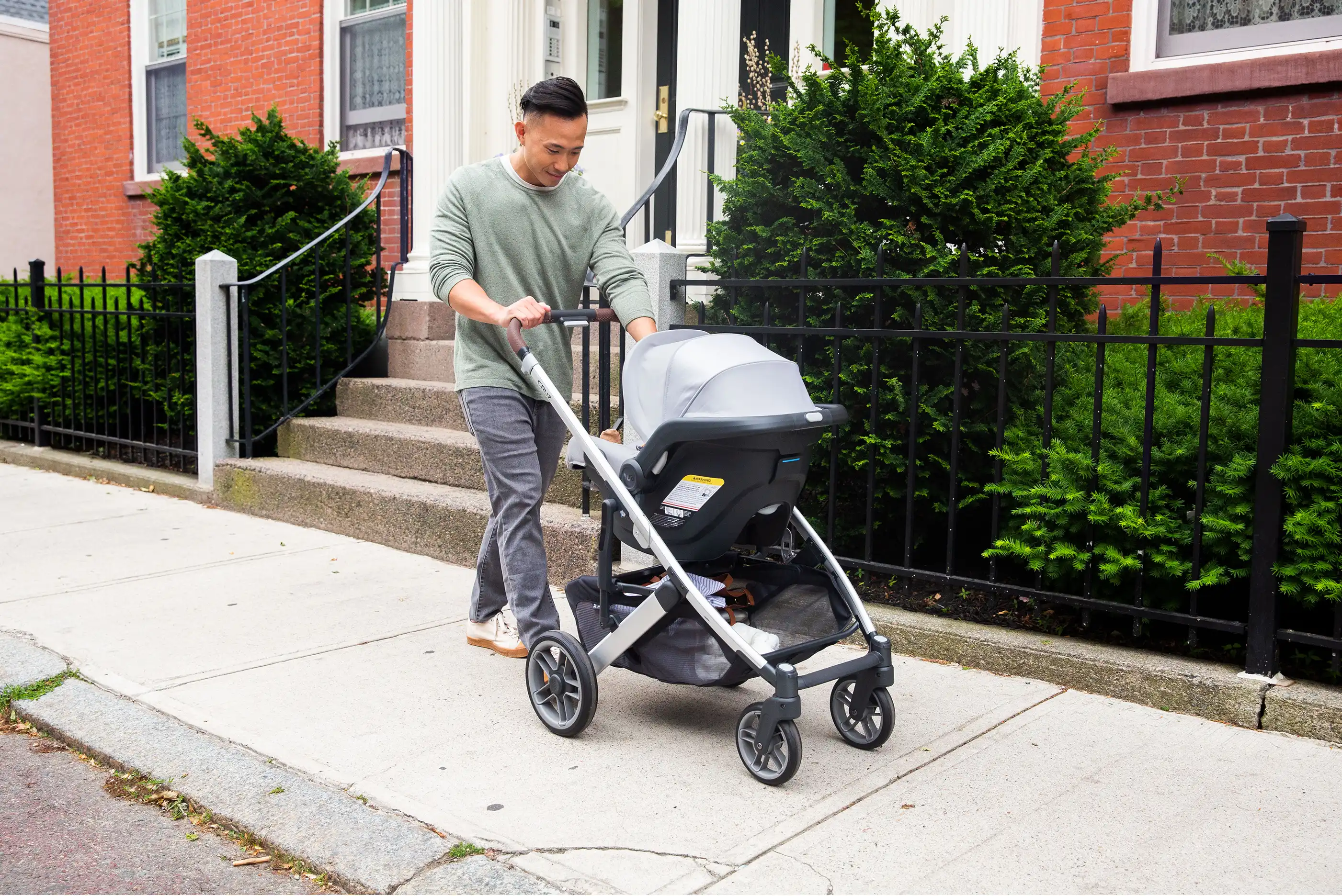 Parent pushes stroller with installed car seat along neighborhood sidewalk