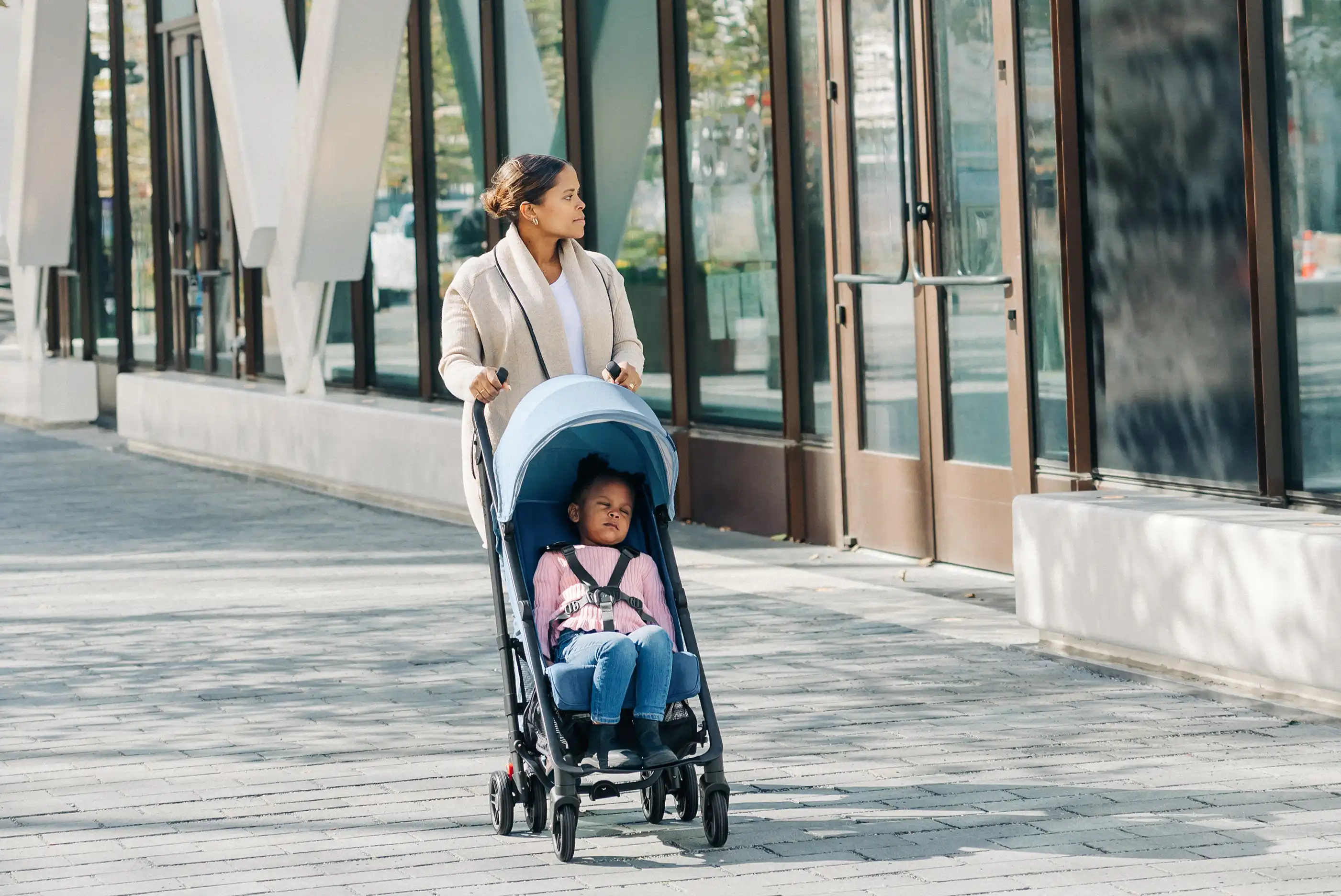 A parent pushes their sleeping child along an urban sidewalk
