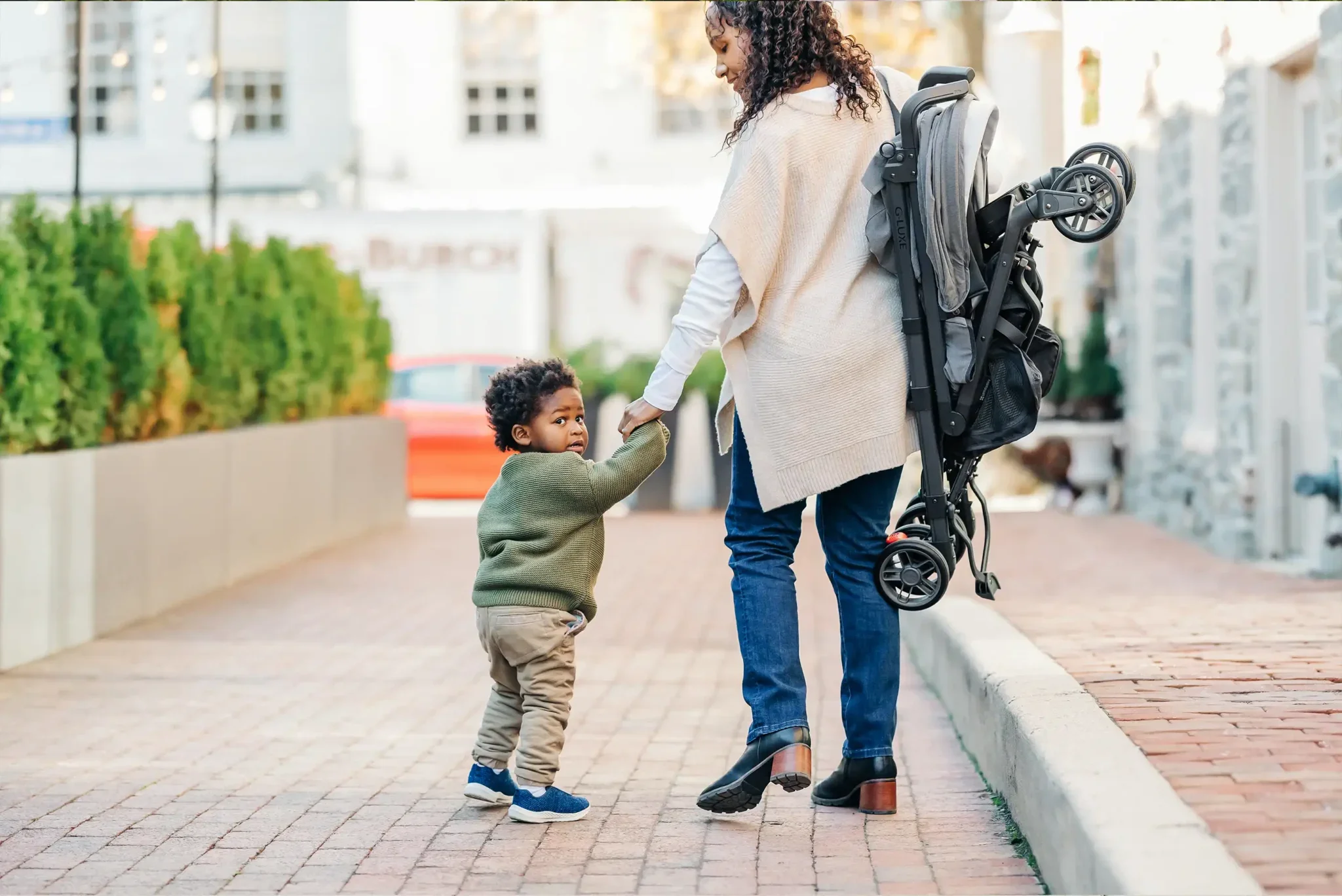 A parent carries their G-Luxe over their shoulder while holding their child's hand